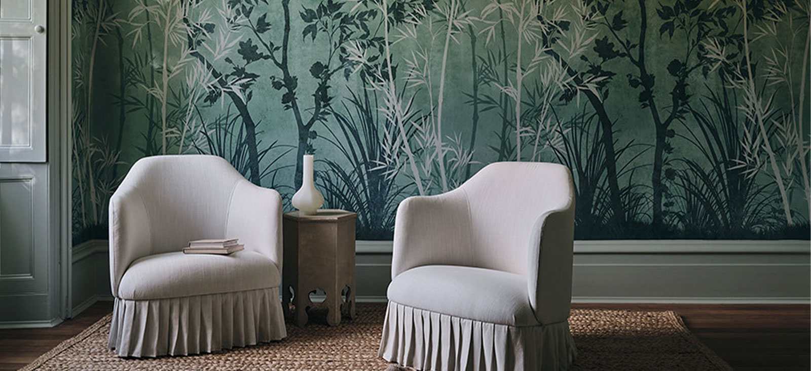 Deep green botanical wallcovering behind two softly tailored white lounge chairs