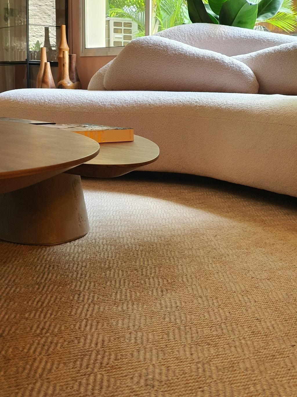 Natural jute rug wrapping a curved sofa and two low wooden tables
