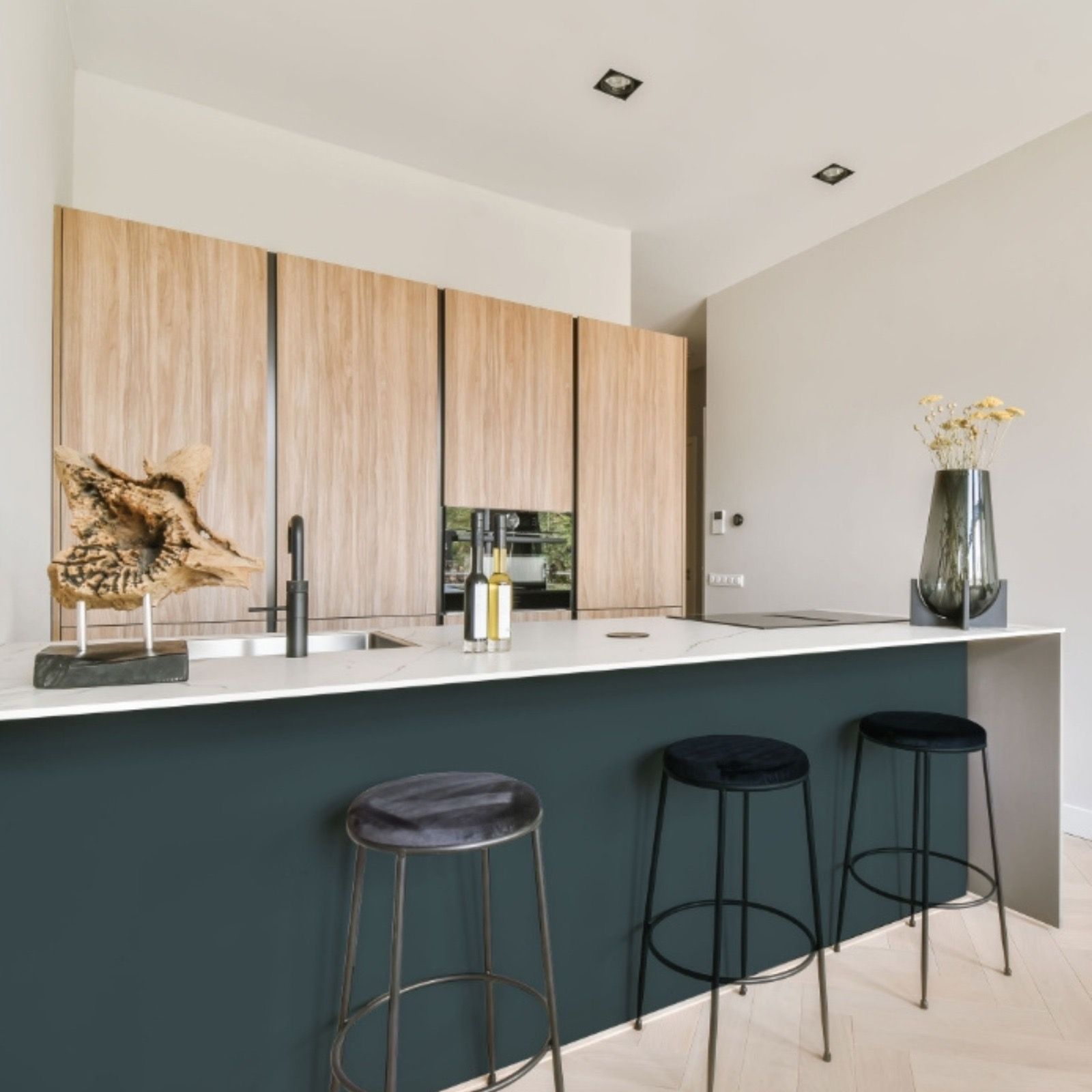 Kitchen island in dark green with pale oak cabinets and a white stone counter