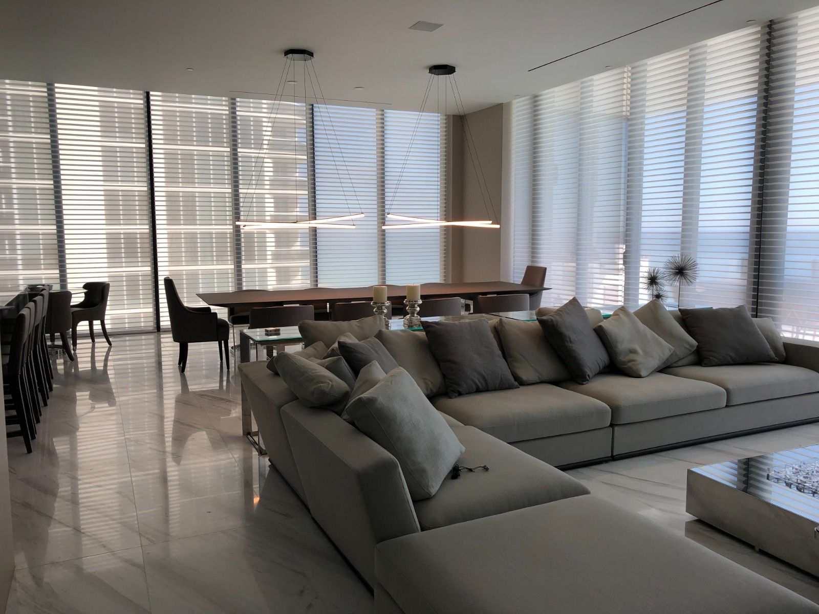 Long living room where screen blinds filter daylight across a grey sectional