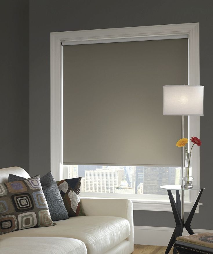 Beige roller shade drawn over a city window beside a pale sofa