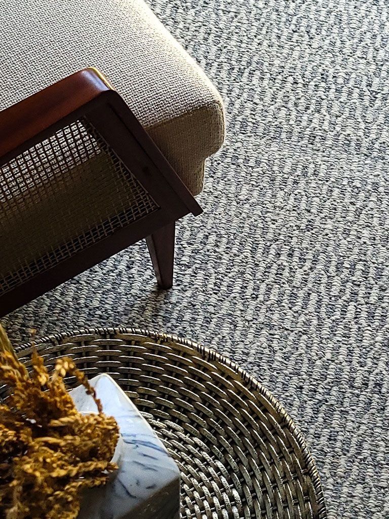 Close weave of a grey-blue rug beside a cane-backed chair and a rattan tray