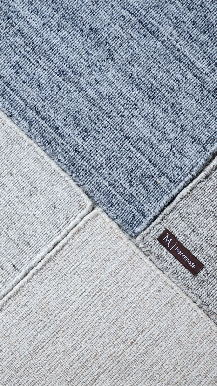 Corner of a grey handwoven rug with the maker label stitched to the binding