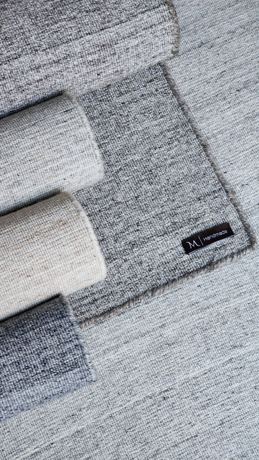 Folded corner of a grey handwoven rug showing the maker label