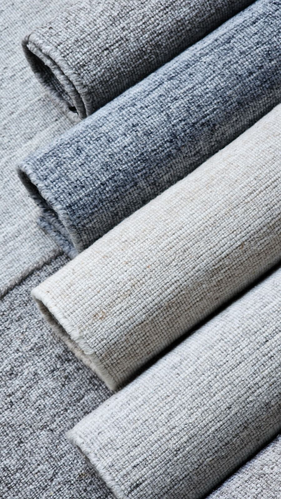 Close-up of three rolled rugs showing grey and ivory handwoven texture